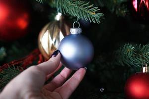 Female hand holds a Christmas ball on background of a Christmas tree
