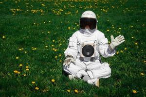 Futuristic astronaut in a helmet sits on a green lawn among flowers photo
