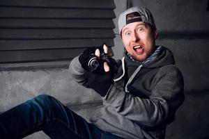 Man with a camera and a funny face sitting on a chair in a gray studio photo