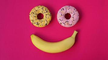 dos donas y un plátano yacen sobre una superficie rosa, formando una emoción de sonrisa foto