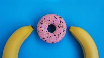 Two bananas and a pink donut blue background. Erotic concept photo