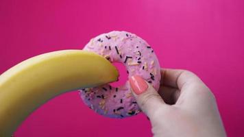 Sweet donut and banana in hand on pink color photo