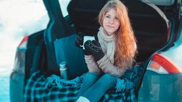 Happy girl sitting on truck of car in winter forest