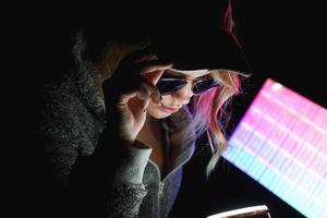 Hacker girl in cap and sunglasses in front of a computer in neon light photo