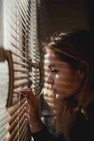 Beautiful young woman looks out through blinds photo