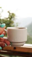 Hand white cup of hot coffee. In the morning, cold mountain views photo