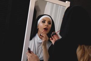 mujer en un traje de monja pinta labios cerca de un espejo