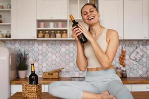 Mujer en un chándal en una cocina ligera bebe vino tinto foto