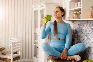 Woman sits on the countertop in kitchen and drinks photo