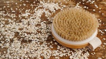 Wooden round massage brush on a wooden background. Scattered oatmeal. photo