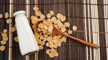 copos de maíz saludables y leche y una cuchara de madera sobre una servilleta de bambú. foto