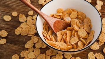 Yellow cornflakes in a white bowl. Wooden spoon
