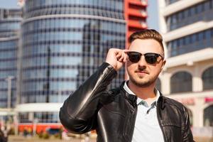 un atractivo hombre vestido con chaqueta de cuero negro con gafas de sol oscuras foto