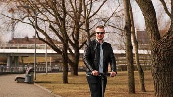 Young man in a black jacket and sunglasses rides an electronic scooter photo