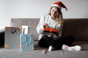 Beauty girl opening present gifts sitting on sofa at home photo