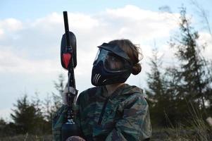 Chica de jugador de deporte de paintball en uniforme de camuflaje protector y máscara foto