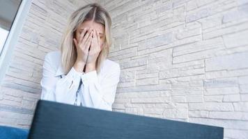mujer mira su computadora portátil con una expresión de preocupación y dolor