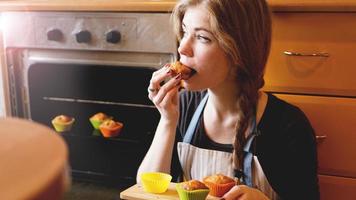 Hermosa mujer rubia mostrando muffins mientras come uno en la cocina