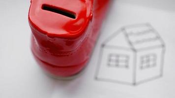 Hand dropping coin into the moneybox. Drawing a house photo