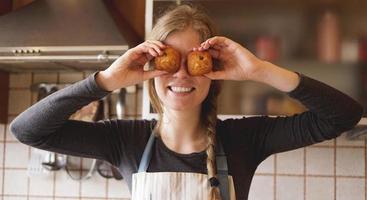 Portrait of beautiful woman in apron covering her eyes with muffins photo
