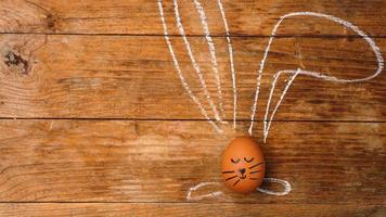 Egg on a wooden background. Chalk-drawn ears and a painted muzzle photo