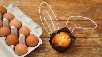 Homemade muffin with painted rabbit ears. Muffin and eggs on a wooden photo