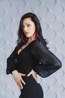 Woman wearing a black dress, red earrings in light studio photo