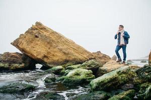 Traveler man with a backpack stands on a rock against a beautiful sea photo