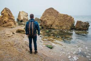 Hombre viajero con una mochila se encuentra en una roca frente a un hermoso mar foto