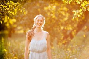 Happy young woman stands in summer apple orchard photo