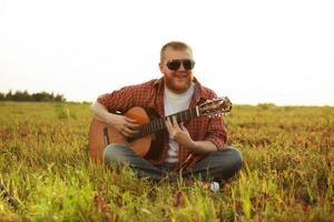 hombre en jeans se sienta y toca la guitarra foto