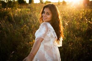 Girl in a dress walks in the field at sunset photo