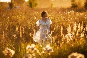 Girl walks through a meadow at sunset photo