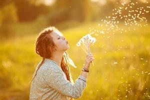 Girl in dreads blowing on dandelion photo