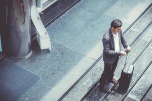 Asian businessman talking phone while walking holding suitcase. photo