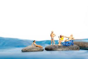 Familia de personas en miniatura sentado en las grandes rocas cerca de la costa foto