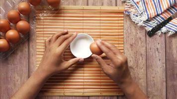 Man breaking egg and pouring into a small container on table , video