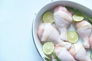 Raw chicken drumstick and slice of lemon in a bowl on white photo