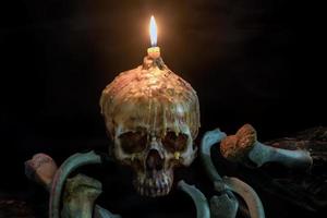 Cráneo con luz de velas en la parte superior y hueso sobre madera grunge foto