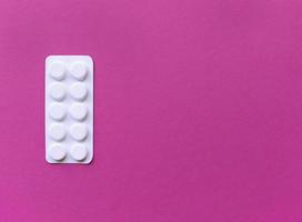 Blister de pastillas blancas sobre fondo de color rosa con espacio de copia