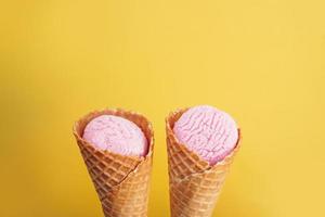 Delicious pink ice cream in a cone on a yellow background. photo