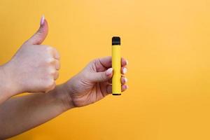 Yellow disposable electronic cigarette in female hand. photo