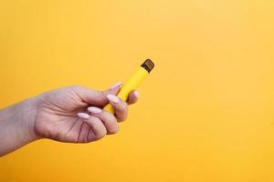 Cigarrillo electrónico desechable amarillo en mano femenina foto