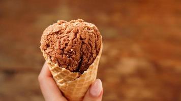 Chocolate ice cream on waffle cone. Wood background. Selective focus. photo