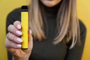 Cigarrillo electrónico desechable amarillo en mano femenina foto