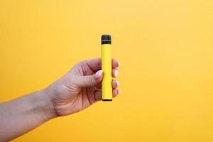 Cigarrillo electrónico desechable amarillo en mano femenina. foto