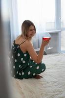 chica en pijama verde en la cama con una copa de vino tinto foto