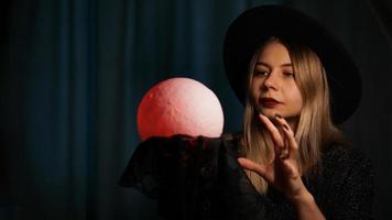 una adivina joven con un sombrero sostiene una bola mágica. foto