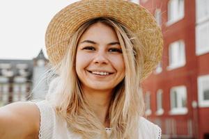 Sonriente joven chica rubia alegre con sombrero haciendo selfie foto