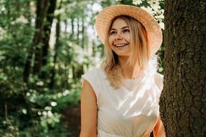 hermosa chica con un sombrero de paja y ropa elegante se encuentra cerca de un árbol foto